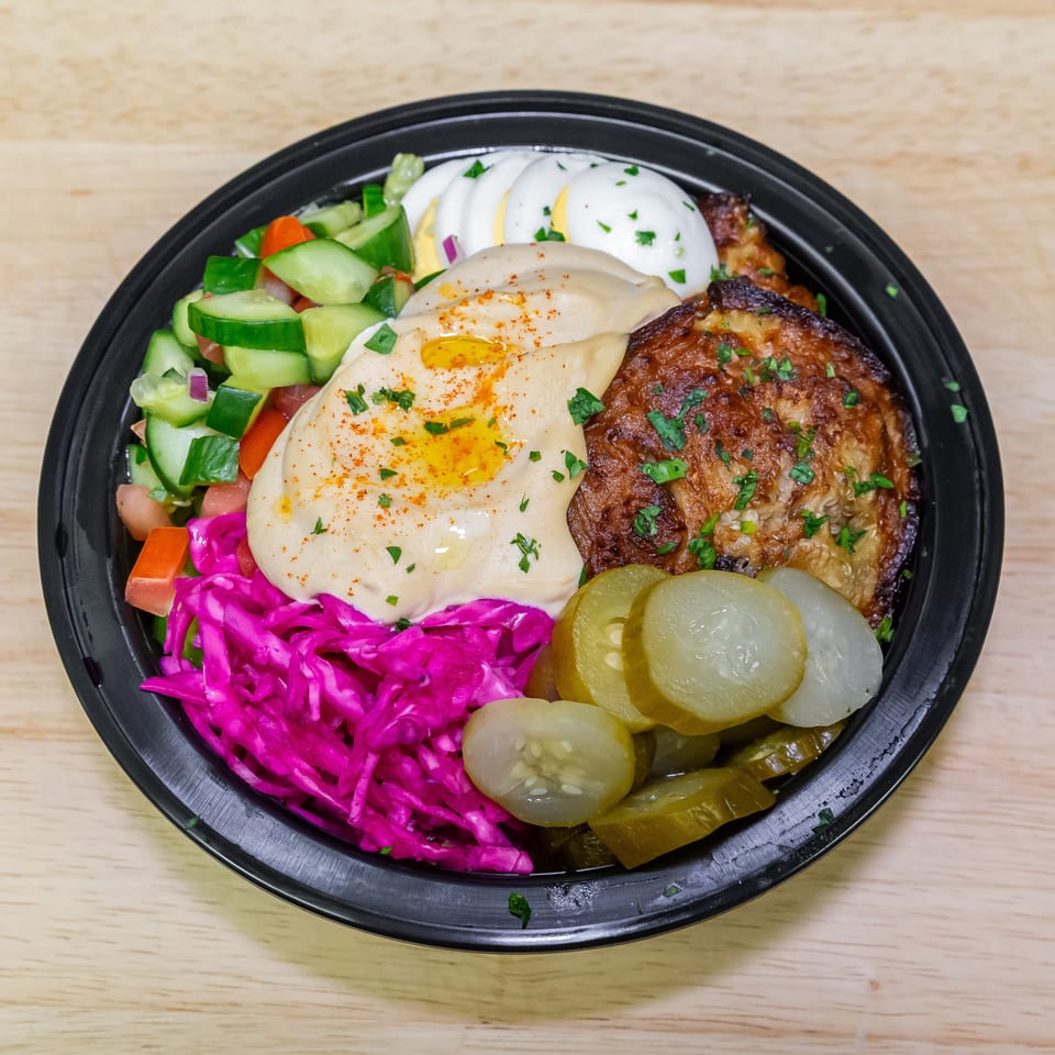 Mediterranean bowl with hummus, grilled meat, boiled eggs, chopped salad, pickled vegetables, and bright purple cabbage.