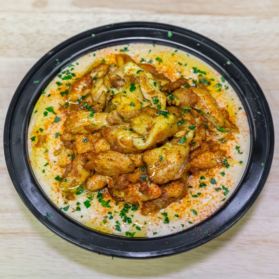 Roasted chicken pieces topped with herbs and paprika, served over creamy sauce in a black bowl.