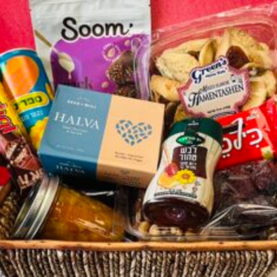 Gift basket filled with assorted packaged Jewish foods, including halva, hamantaschen, snacks, preserves, and a bottle.