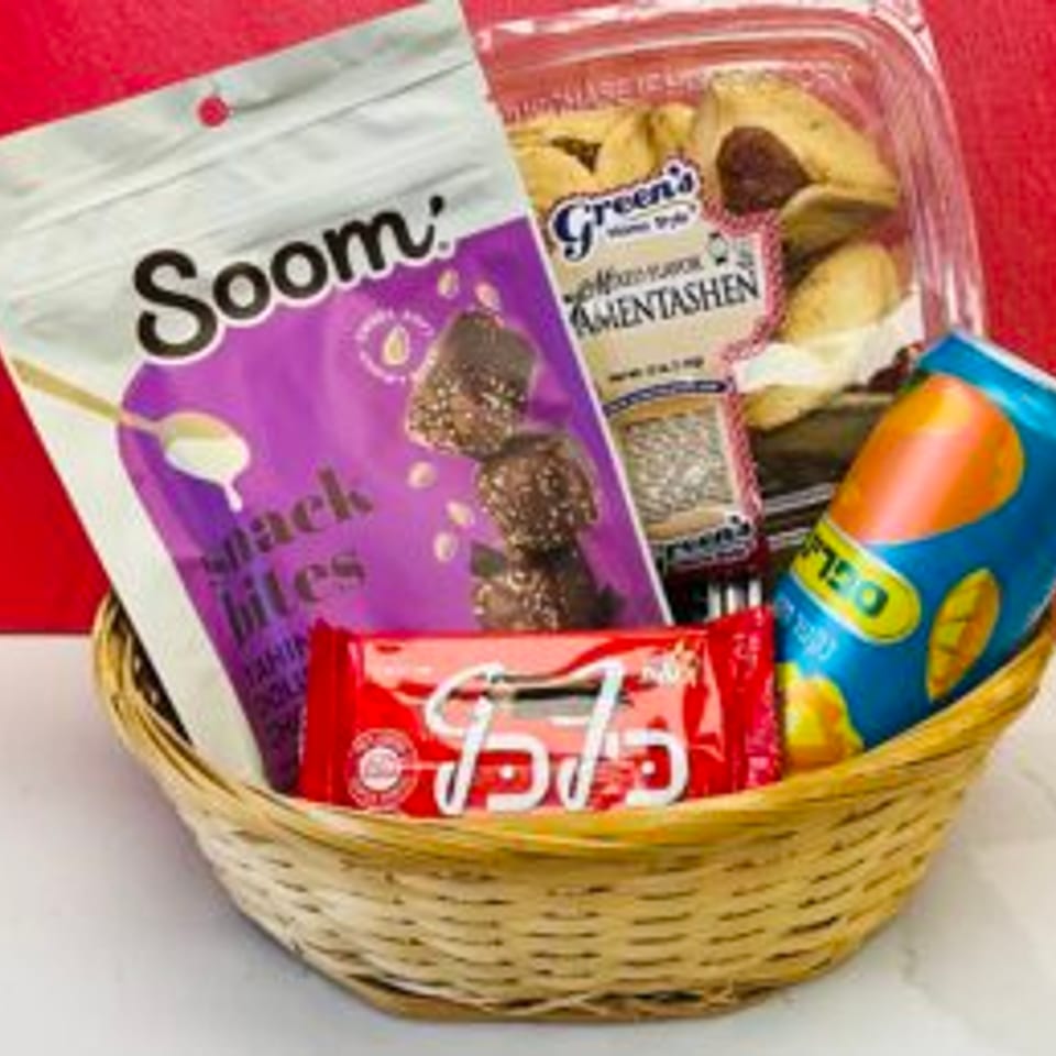 Woven basket filled with assorted packaged snacks, chocolate treats, wafers, and a colorful soda can against a red background.