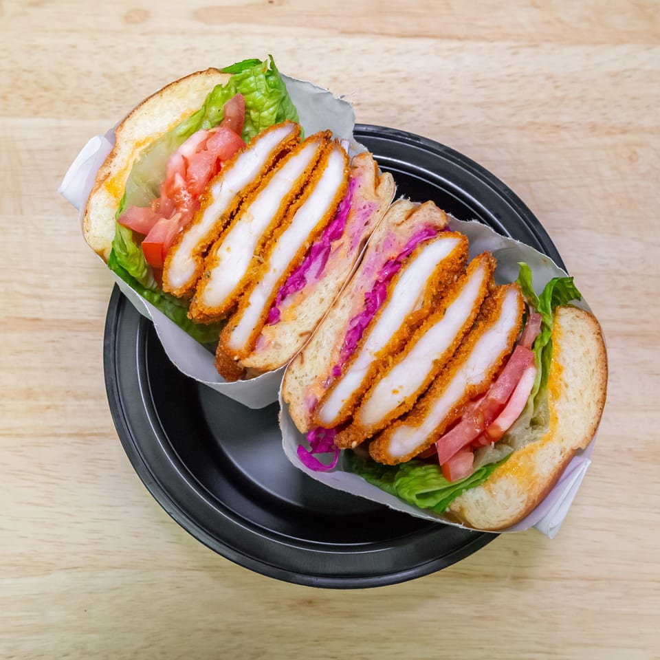 Two crispy chicken sandwiches with lettuce, tomatoes, and purple cabbage sit on a black plate.
